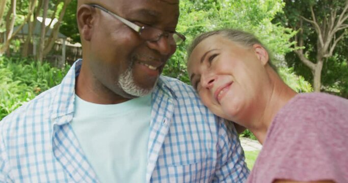 Happy senior diverse couple wearing shirts and embracing in garden