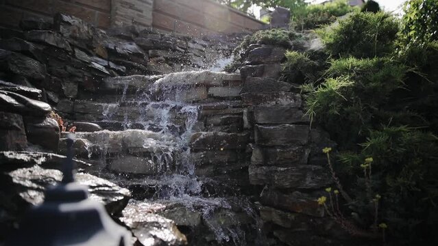Decorative waterfall at home garden. Garden pond with waterfall. Exterior of a private garden. Pool with rocks and waterfall. Landscape design of the backyard in summer