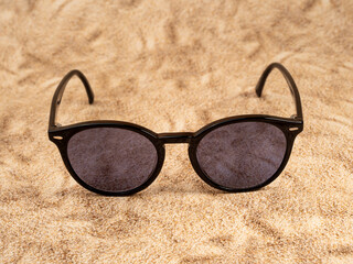 Stylish sunglasses. Sunglasses in a dark frame on a sandy background. Close-up.