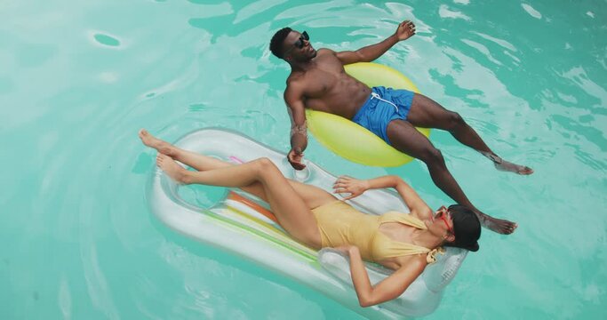 Happy diverse couple wearing swimming suits with inflatables at swimming pool in garden