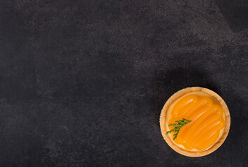 Round tartlet with custard tangerine cream and curly tangerine jelly on top. Dark grey background. Top view. Copy space