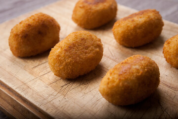 Classic Spanish croquettes on wooden board with dim light in the background. Fried potato.