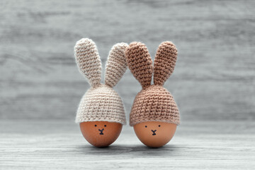 Two Easter eggs in crochet hats with bunny ears against painted shabby wooden background