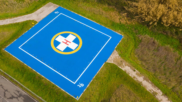 Aerial Closeup Of A Helicopter Landing Pad Near Emergency Hospital And Medical Centre. A Blue Asphalt-covered Helipad With A Special Symbol In The Center For Helicopter Landing, Near A Green Field. 