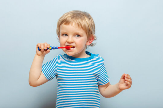 Little blonde boy brushing teeth with toothbrush on blue background