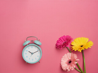 Spring time concept green alarm clock next to pink, fuchsia and yellow flowers