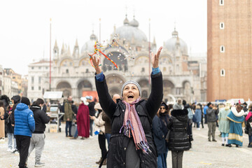 Happy woman in winter clothes smiling and throwing confetti at San Marco Square during 2023 Venice carnival celebrations