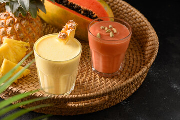 Pineapple and papaya lassie or smoothie in tray on black background. Traditional Asian beverage of pineapple, papaya and ice. Close up.