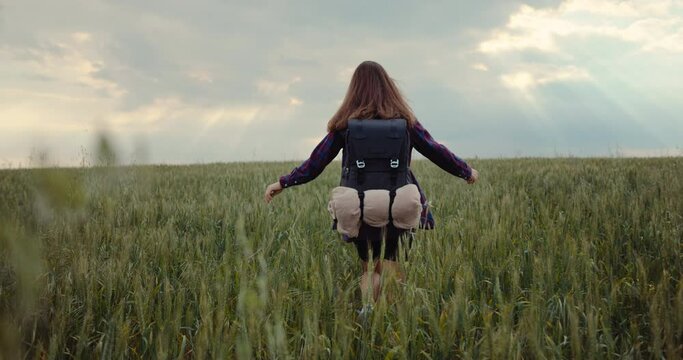 A woman is hiking with a backpack on a green field. A dreamy girl walks in nature and feels pleasure and freedom. High quality 4k footage