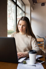 Young  woman working with laptop while sitting at cafe indoors
