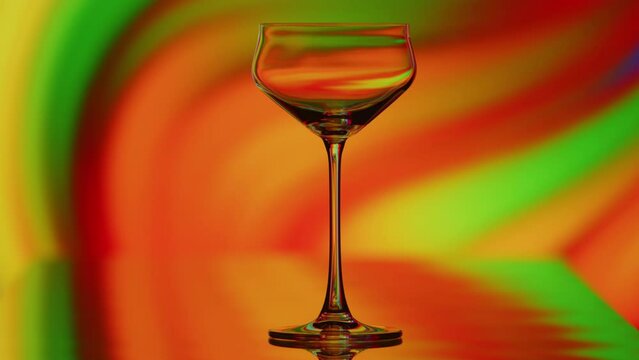 The clear glass is standing infront of a colorful curvy rainbow background. The reflactions warp with the shape of the glass. High quality 4k footage