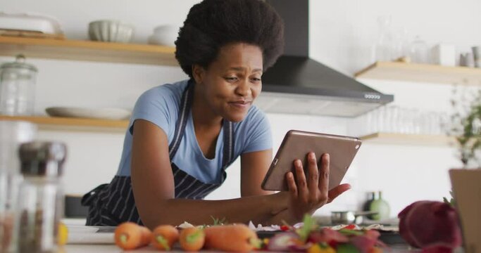 Happy african american woman preparing dinner using tablet in kitchen