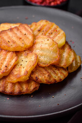 Delicious crispy fried potatoes in slices on a black ceramic plate