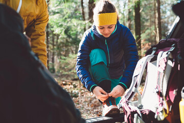 Woman hiker tying up her shoes at the car trunk, going for a hike