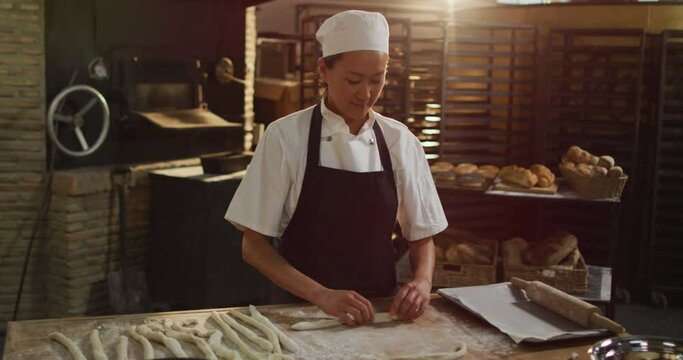 Animation of happy asian female baker preparing rolls at bakery