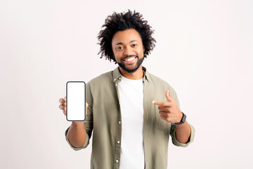 Attractive 30s african-american man pointing finger at smartphone with blank empty screen standing...
