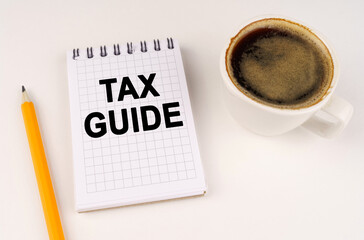 On a white surface, a cup of coffee, a pencil and a notepad with the inscription - TAX GUIDE