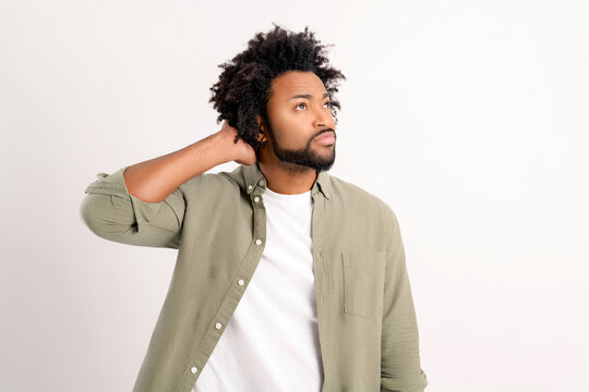 Puzzled African-American curly guy holding hand on the back of the head standing isolated on white lost in doubts, man immersed in thinking or making important decision, solving problem