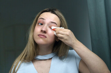 A young woman cleans her eyelids with napkins.