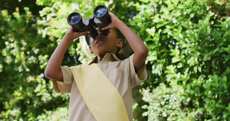 Animation of african american girl in scout costume using binoculars in garden