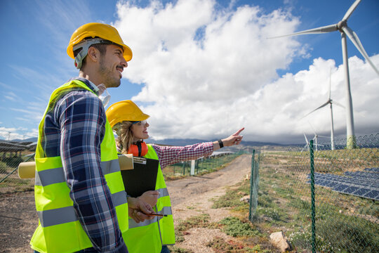Two engineers are having a conversation while observing wind turbines, renewable energy concept