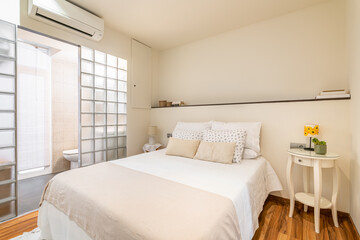 Cozy white bright small bedroom with bed and glass block wall with private toilet with vanity and air conditioning. Hotel room concept. Honeymoon Budget Room