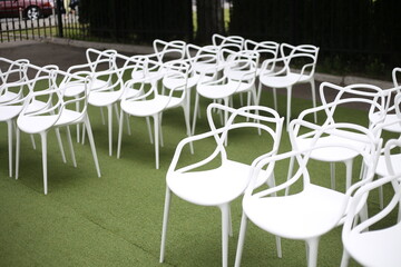 White elegant plastic chairs stand prepared for the wedding ceremony on the green lawn