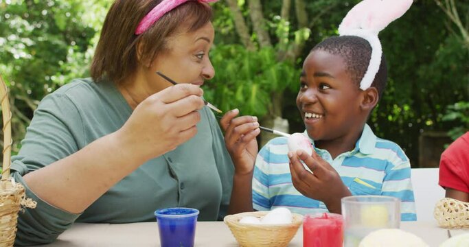 Animation of happy diverse grandmother and grandson painting easter eggs in garden