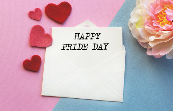 An open envelope with the text HAPPY FRIDE DAY , on a pink and blue background with a decor of felt hearts and a flower. Flat lay, top view. LGBT concept.