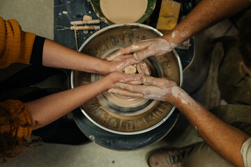 Top view man and womans hands making form from clay on pottery wheel. Master class, workshop,...