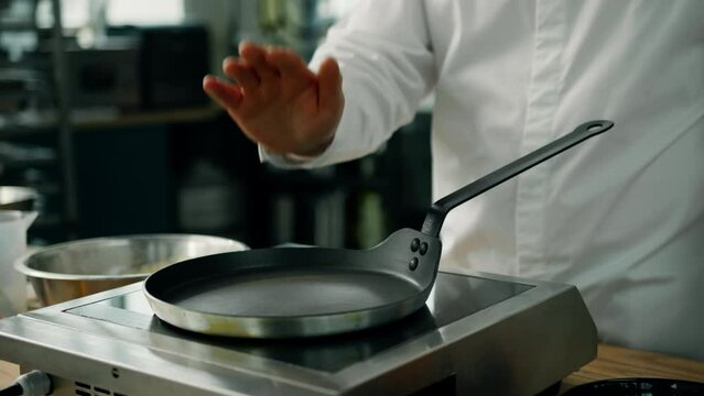 Professional kitchen: chef checking a pan on professional stove for cooking pancakes
