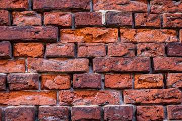 A unplastered weathered brick wall captured in a close-up, with hues ranging from red to purple and...