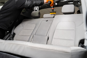 Applying detergent on textile seat in car interior for dry cleaning. Smearing detergent on car textile seats using drill with brush for dry cleaning.