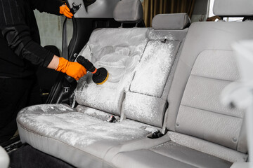 Smearing detergent on car textile seats using drill with brush for dry cleaning. Applying detergent on textile seat in car interior for dry cleaning.
