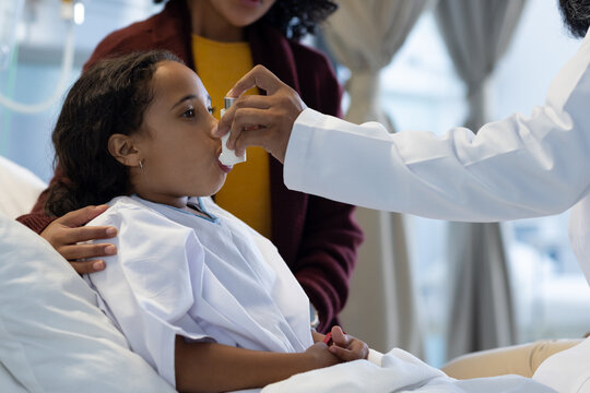 Diverse male doctor examining sick daughter with mother on hospital bed