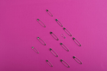 A pattern of silver safety pins of different sizes and shapes laid out in rows, on a bright pink...