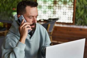 Thoughtful young adult man in casual clothes in cafe talking on a mobile phone