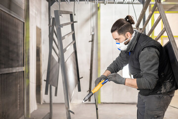 An adult man working in a factory finishes a job using the technique of electrostatic powder...
