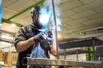A man working as a welder with a protective mask and work clothes performs vertical work with a...