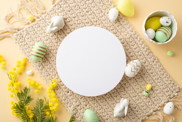 Easter concept. Top view photo of empty white circle bowl with colorful easter eggs ceramic bunnies cloth napkin and mimosa flowers on isolated beige background with blank space