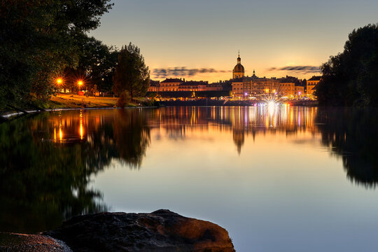 Chalon sur Sa&ocirc;ne bei Sonnenuntergang. Die Altstadt reflektiert auf der spiegelglatten Wasseroberfl&auml;che. Lichter erhellen die Uferpromenade