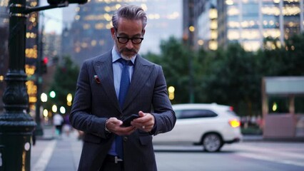 Business man in expensive tailor-made suit walks down city street and looks at screen of a mobile phone device, he is in large metropolis. Successful businessman reads email in handy smartphone app - Powered by Adobe
