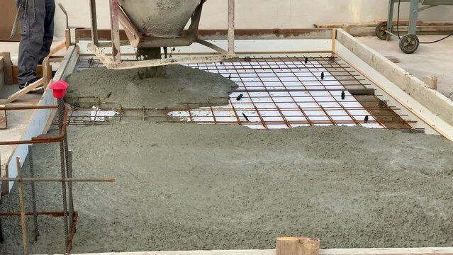 Construction worker pouring concrete on a reinforced slab with a bucket. Reinforced concrete on a construction site with a worker wearing safety boots and clothes.