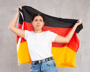 Sad young female student in casual wear with flag of Germany against of gray wall background