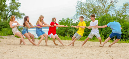 a group of teenagers playing tug of war on the beach