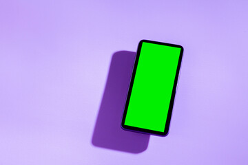 Smartphone with green screen on top of a purple table. smartphone concept. Green screen concept.