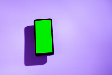 Smartphone with green screen on top of a purple table. smartphone concept. Green screen concept.