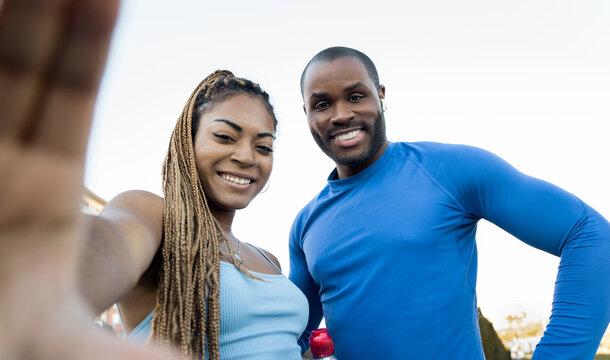 Healthy lifestyle concept. Dark-skinned millennial couple doing outdoor sports together, man and woman happily take a picture with the mobile from below to save for memory.