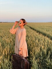 girl in a field of green wheat with a suitcase in her hands