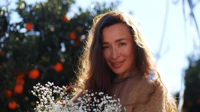 Beautiful smiling woman holds white flowers in the orange garden